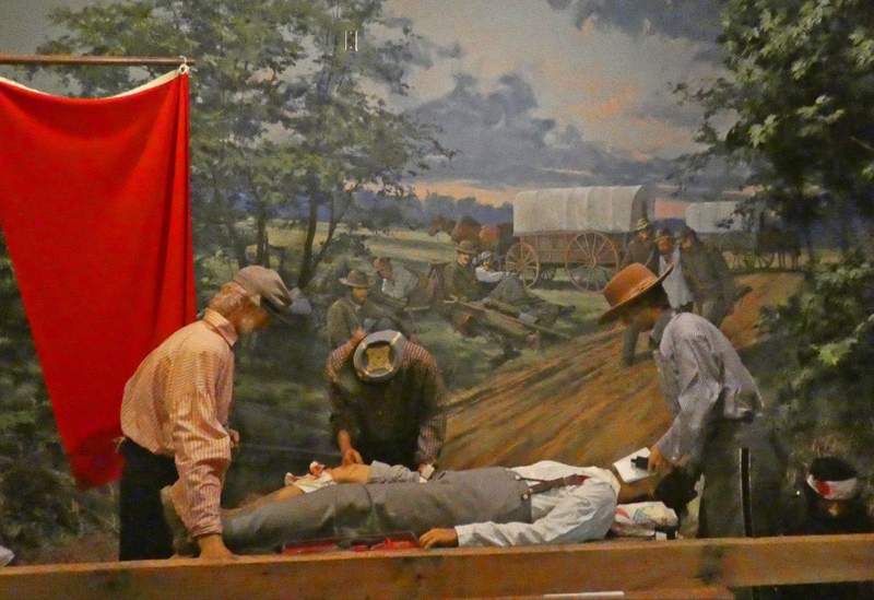 A  live like exhibit of a Civil WAr era doctor preparing to amp outate a soldiers leg  with an assistant administering ether and another at the patient's foot.