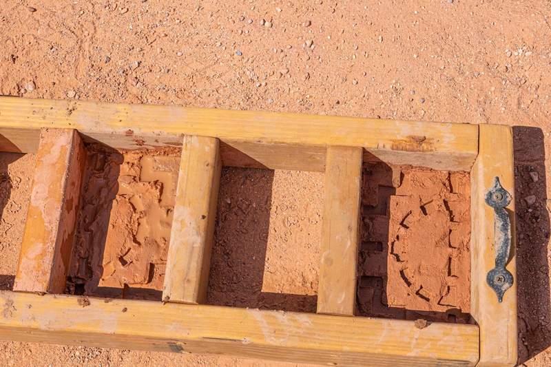 Wooden adobe brick molds filled with wet clay and straw sit on sandy ground beside a white bucket during a traditional brick-making activity at the Hyatt Regency Tamaya Resort & Spa.