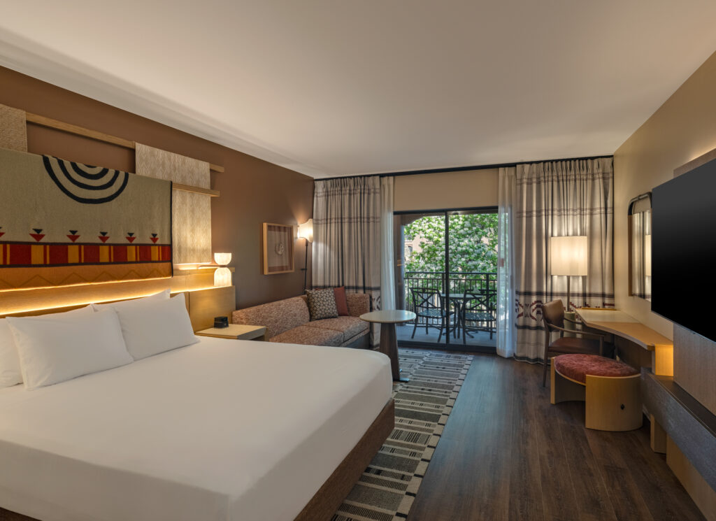 A renovated guest suite at the Hyatt Regency Tamaya Resort & Spa featuring a king bed, a sitting area with a sofa, and a private balcony. The décor combines Pueblo-inspired textiles, warm desert tones, and natural wood accents for a modern Southwestern feel.