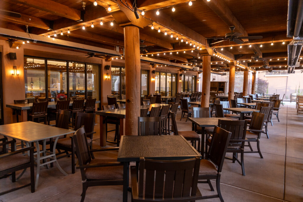 The outdoor patio of the Santa Ana Café at the Hyatt Regency Tamaya Resort & Spa glows under string lights. Wooden beams, adobe walls, and sturdy tables create a warm, Southwestern ambiance for casual dining.
