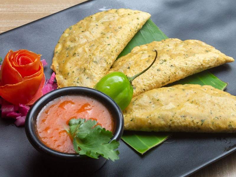 Plate with 3 corn empanadas accompanied by tomato sauce and an habanero chili.