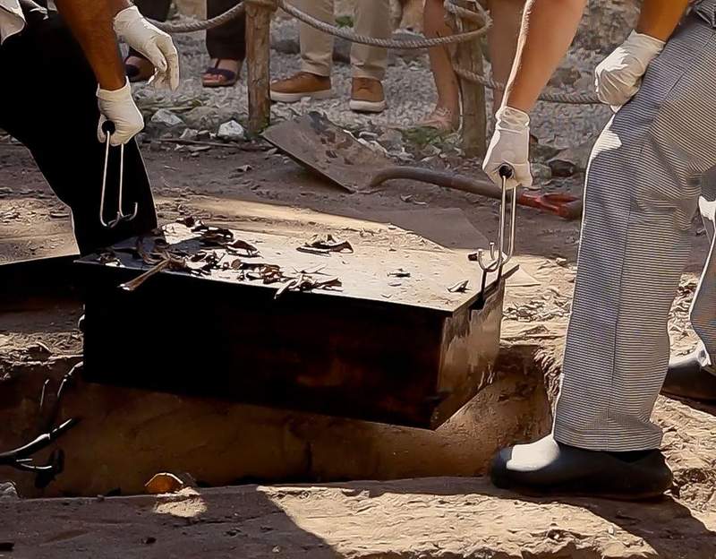 Two men seen digging up a metal container from the ground.