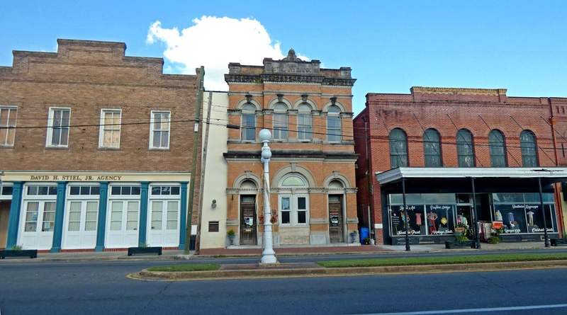 Three turn of the century buildings with a white gas lamp typestreet post.
