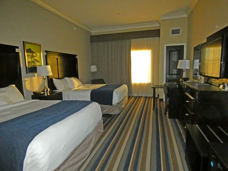 Hotel room with two beds, desk and dresser and large window.