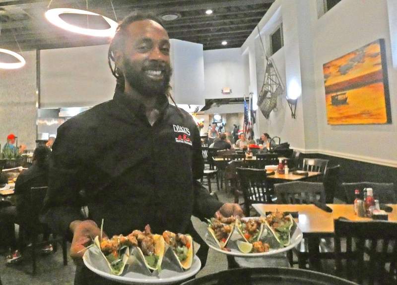Server holding two dishes of tacos in restaurant.
