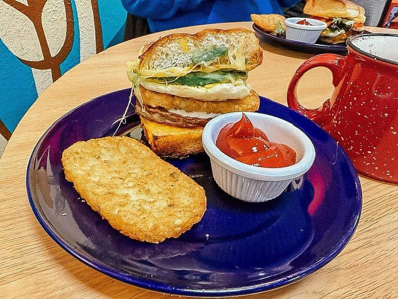 Breakfast sandwich on a blue plate with a bowl of ketchup