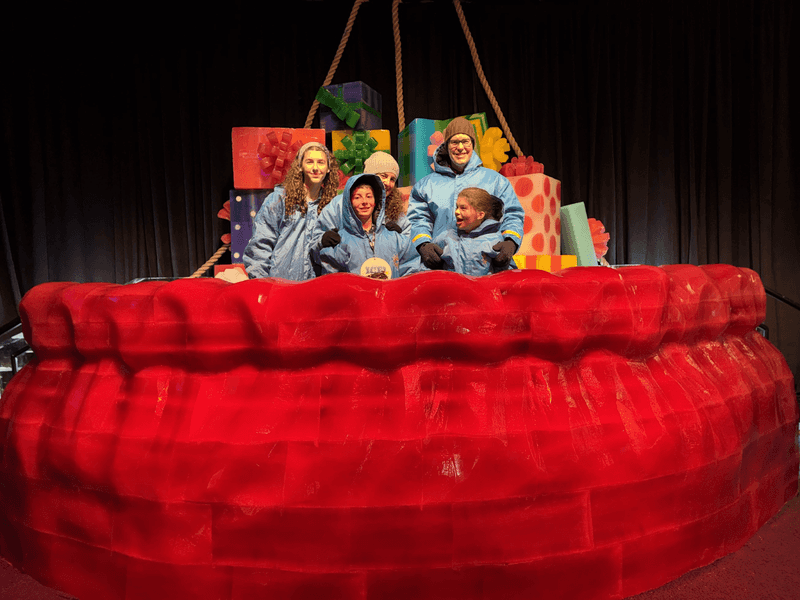A family wearing blue parkas standing in red ice sculpture. 