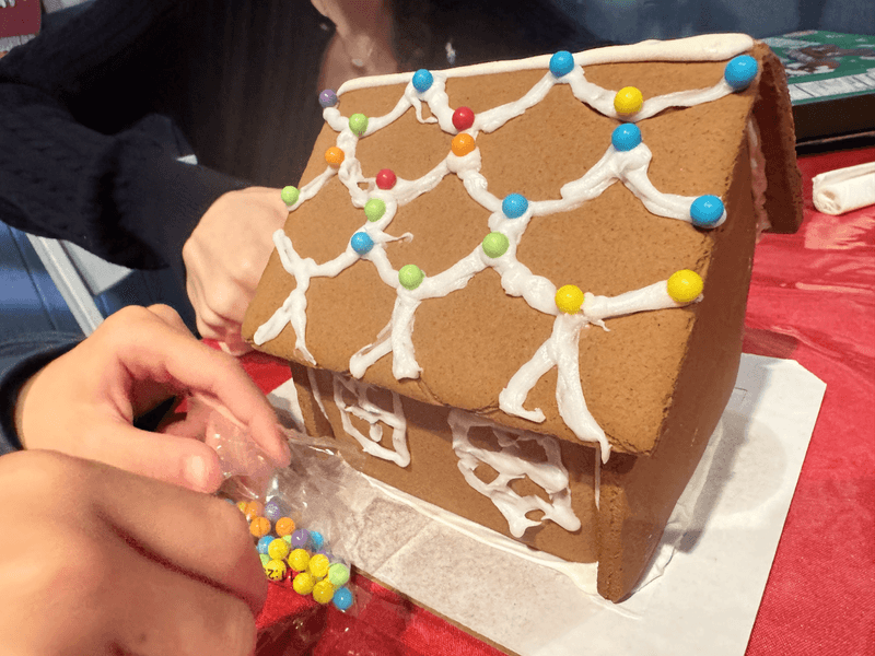 Close-up of a gingerbread house that two children are decorating. 