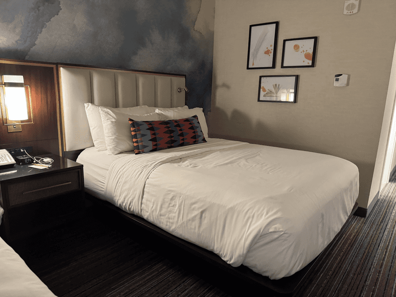 A hotel room with a bed with white linens and a blue wall. 