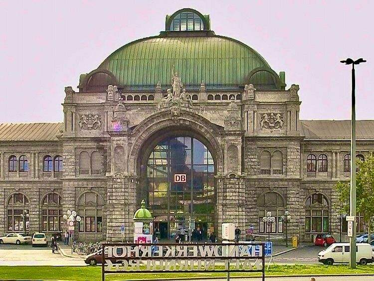 Exterior of Nürnberg Hauptbahnhof showing its historic architecture with a green copper dome, large central arched window, and detailed façade.