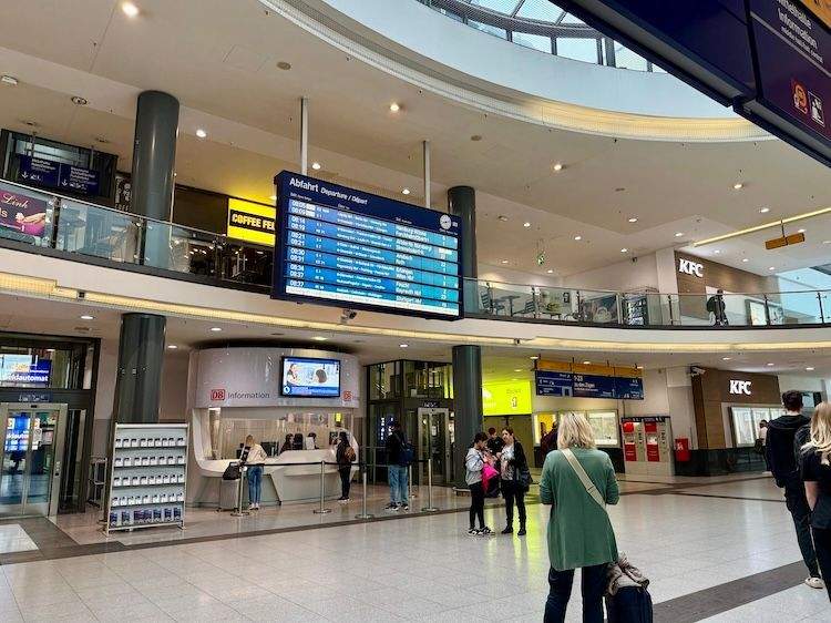 Interior of Nuremberg Central Station’s main entrance, showing passengers walking and looking at the train schedules.
