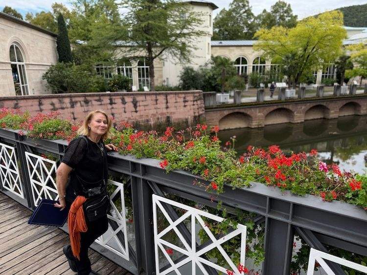 Author standing on a bridge above the Fränkische Saale in Bad Kissingen, with paths, gardens, and calm river waters visible.