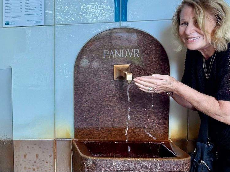 Author tasting water from the Pandur Spring with cupped hands in the Brunnenhalle, the historic spa hall in Bad Kissingen, Germany.