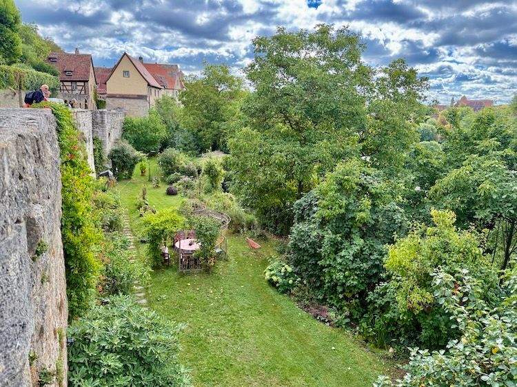 View from Rothenburg ob der Tauber’s city wall, showing the Burggarten and surrounding historic gardens with green lawns and flower beds beyond the medieval walls.