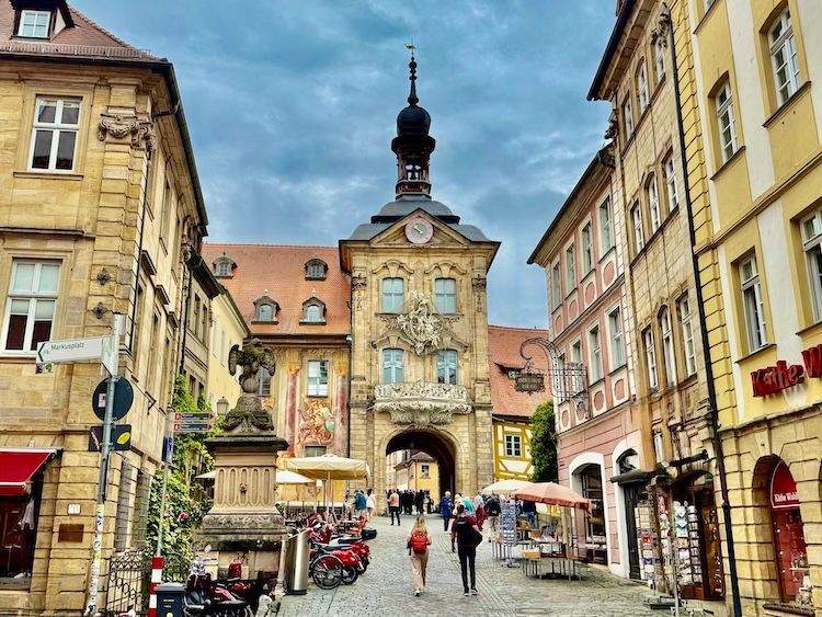 Street view of Bamberg Old Town leading to the Altes Rathaus, showing the building’s decorative façade, clock tower, and archway over the river.