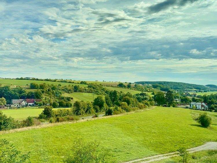View of lush fields, scattered farmhouses, and hills in Bavaria, taken from a moving train near Nuremberg.