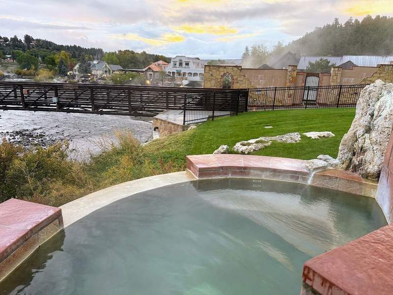 A geothermal heated mineral water pool at The Springs Resort in Pagosa Springs, Colorado, overlooks the San Juan River and the walking bridge connecting the resort to downtown.
