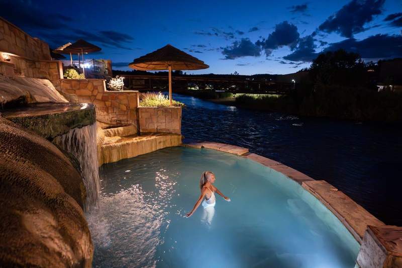 A nighttime soak at dusk at The Springs Resort in Pagosa Springs, Colorado, in an illuminated geothermal mineral soaking pools is enjoyed by a woman.