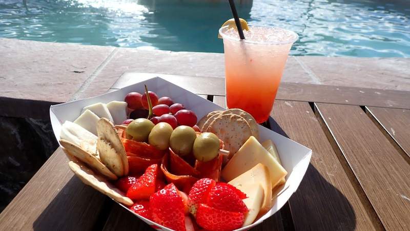 A box of meat, crackers, fruit and cheese with a red beverage next to a pool at The Springs Resort in Pagosa Springs, Colorado.