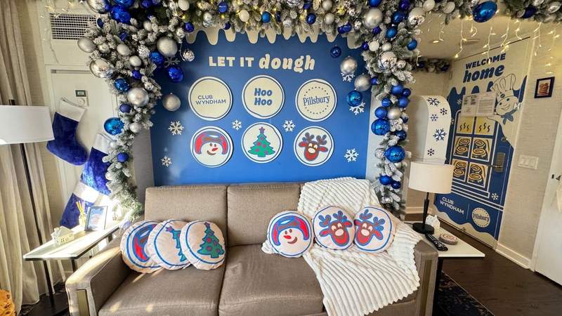 Sofa with six cookie themed throw pillows and a blue and white Pillsbury backdrop with an ornament garland at the Let It Dough suite in NYC.