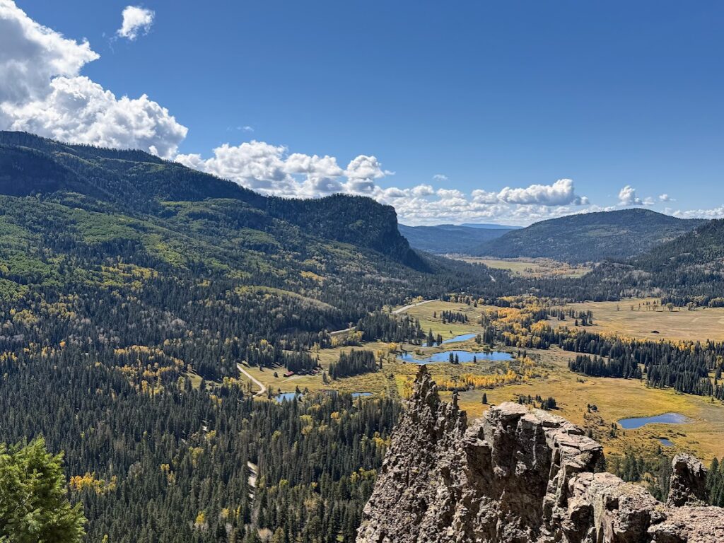 A scenic view from the Wolf Creek Pass near Pagosa Springs, Colorado, overlooks the beauty of the valley below during fall with golden aspen trees and pines sprinkled among rock ledges and lakes below.