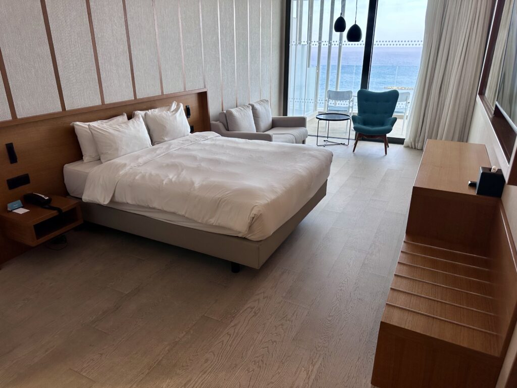 Minimal king bedroom at Radisson beach resort in Laranaca, Cyprus, with blue wing chair near balcony door.