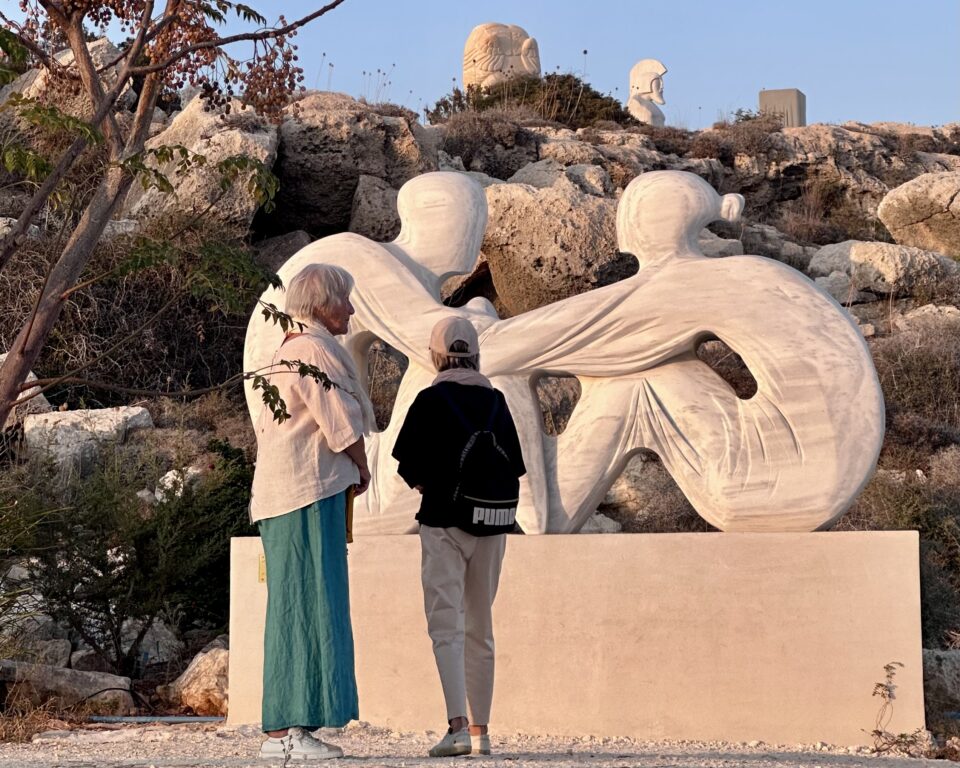 Two women in front of modern sculpture of figures embracing in Ayia Napa sculpture park, a top thing to see in Cyprus