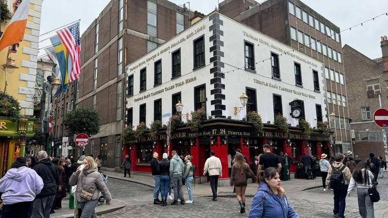 people walking in temple square in dublin infront of a white and red building on a corner.