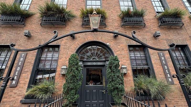 exterior shot of The Dean hotel with black windows, a curved doorway and green shrubs. 