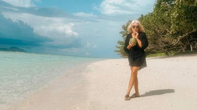 woman drinking a coconut on a tropical beach while traveling full time