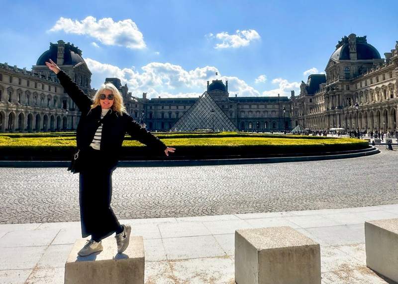 woman standing in front of the Louvre Museum in Paris during a solo visit