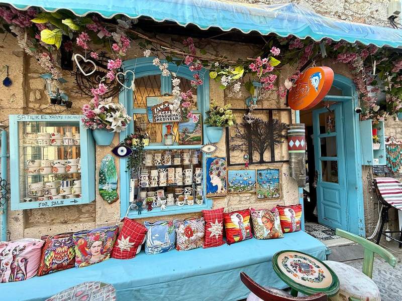 A colorful shot front with turquoise blue trim, a bench with pillow, and wares showcased in display boxes in Izmir Tũrkiye.