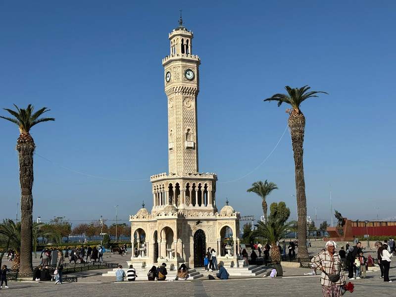 Moorish style clocktower rising above Konak square  with palm trees and people milling about in Izmir.