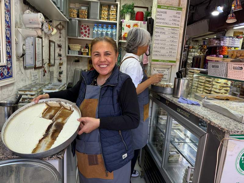 Women and proprietress of sweets shop offering up her fresh made kazandibi in Kemeralti bazaar.