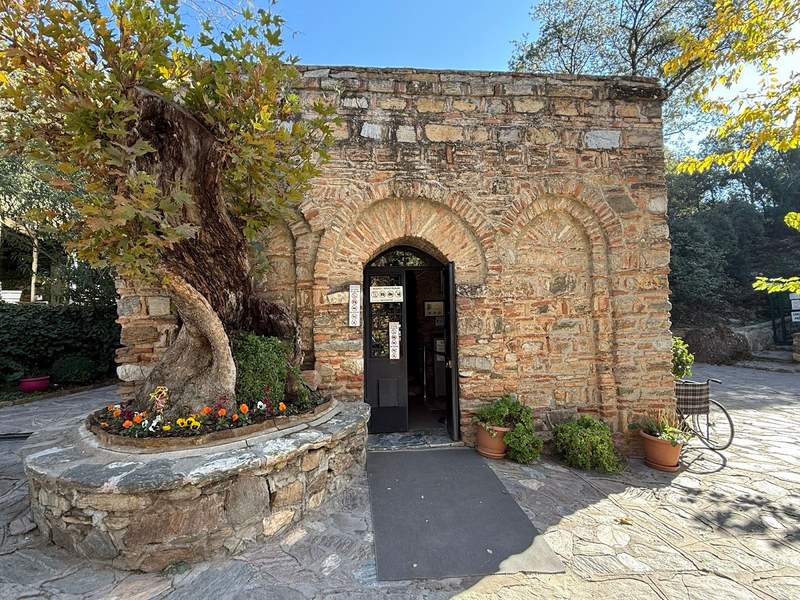 Small, ancient square building with some trees and potted plants around entryway at the House of the Virgin Mary.