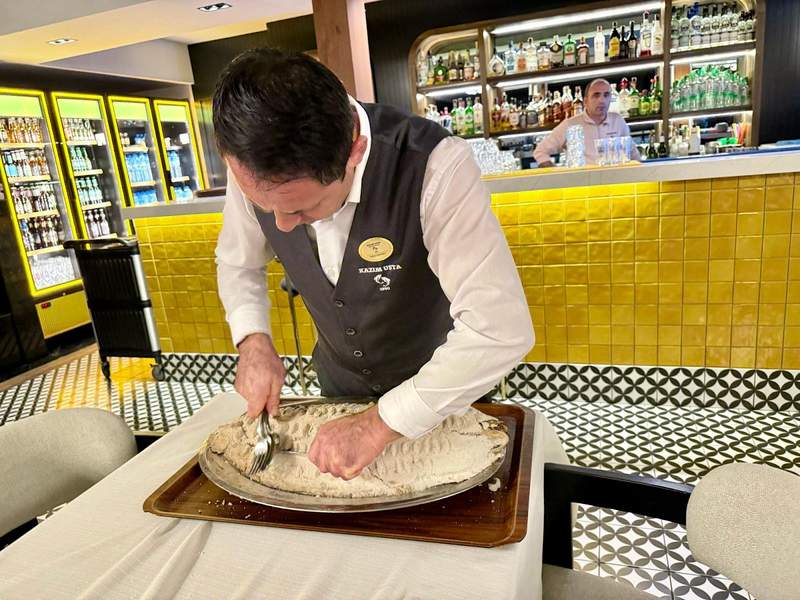 Waiter cracking open the salt shell of a Salt-baked Fish at Kazim Usta Restaurant.