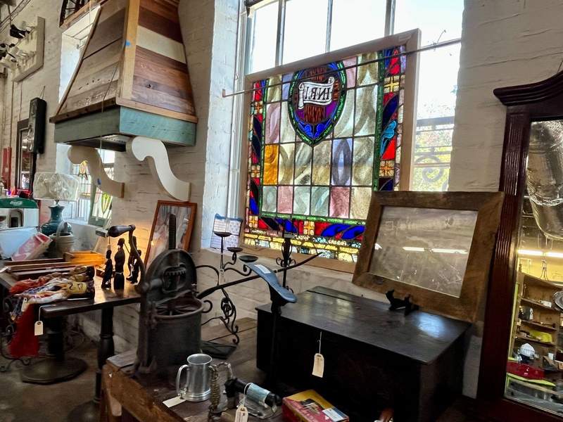 Stained glass window, wooden chest, metal candleholder and other antiques inside Black Dog Salvage store. 