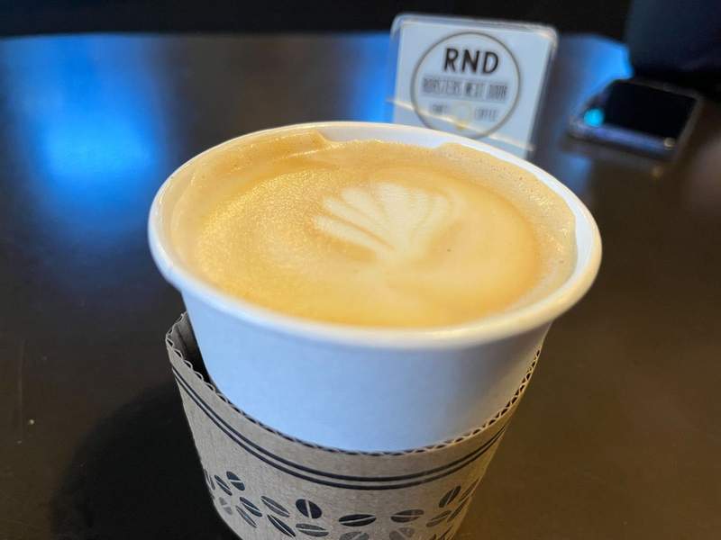A white cup holds a coffee with latte art swirled on top. 