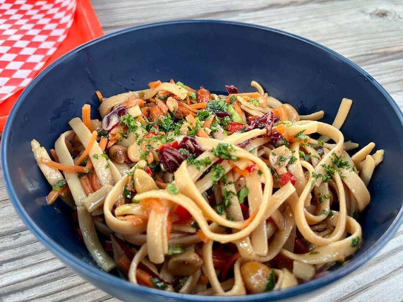 A blue bowl filled with noodles, peanuts and carrots sits on a wooden table. 