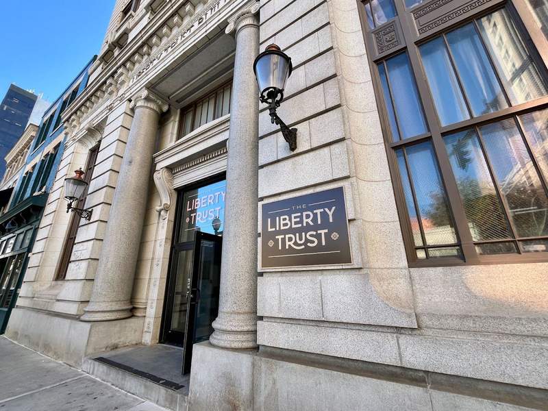 Front of gray stone building with columns, street lamp and a Liberty Trust sign. 