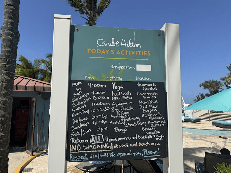 A blackboard showing activities available at the Caribe Hilton with the pool in the background. 