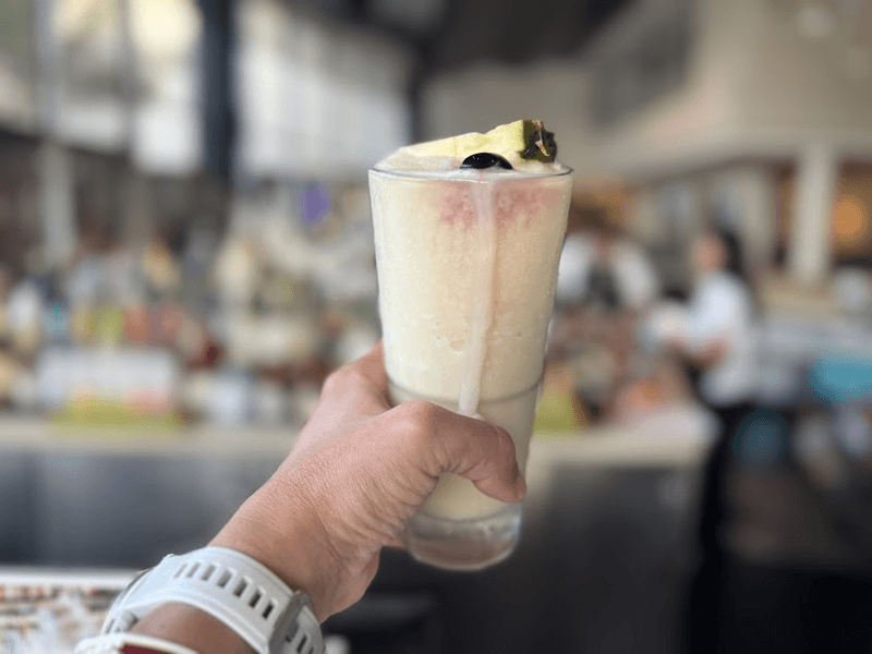 A hand holding a Pina Colada in a glass with a bar in the background. 
