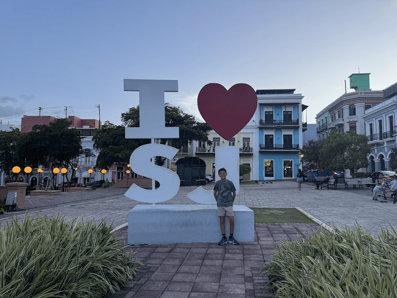 Young boy in short and a t-shirt in front of a sign that says 