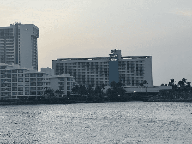 A view of the Caribe Hilton hotel with water in the foreground. 