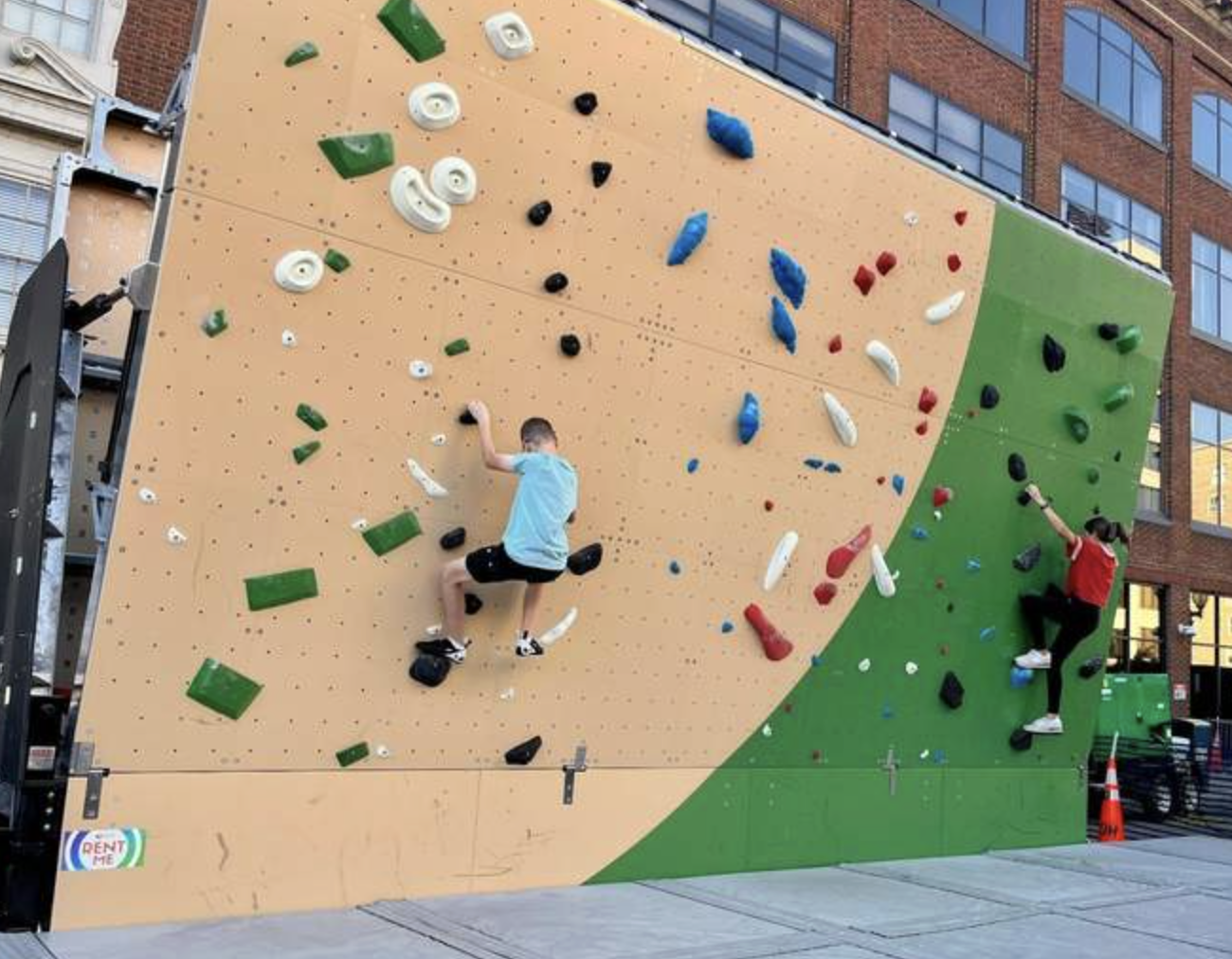 Two children climb an outdoor bouldering wall