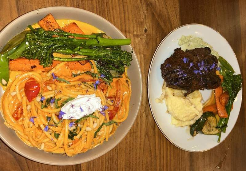 A red pasta dish with fresh green and orange vegetables is on the left. Brown bison meat with mashed potatoes and colorful locally-grown vegetables on the plate on the right.