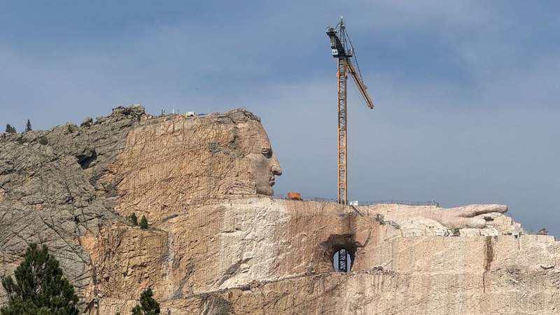 carving of a man on the side of a mountain in south dakota next to a yellow crane.