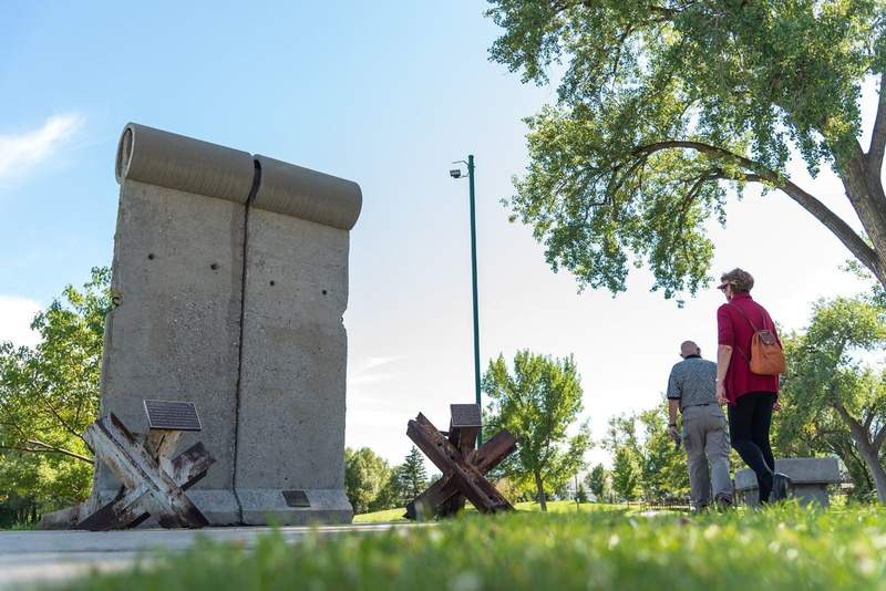 two pieces of the berlin wall next to plaques inside of a park with people walking by in south dakota