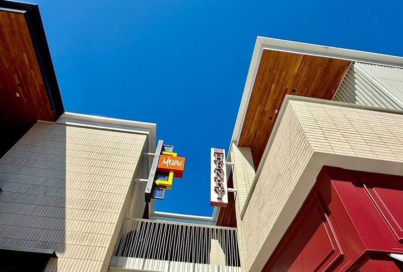 Tops of two sinple, straight line buildings bump into blue sky. A connecting balcony joins them close to the top.
