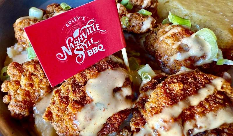 A red flag on a large toothpick declares in white letters: Edley's Nashville style BBQ. Pulled pork is drizzled horizontally with cheese.